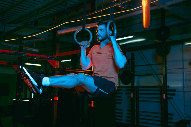 Νεαρός αθλητικός άνδρας, προπόνηση γυμναστή σε γυμναστήριο με μικτό φως νέον. - Φωτογραφία, εικόνα