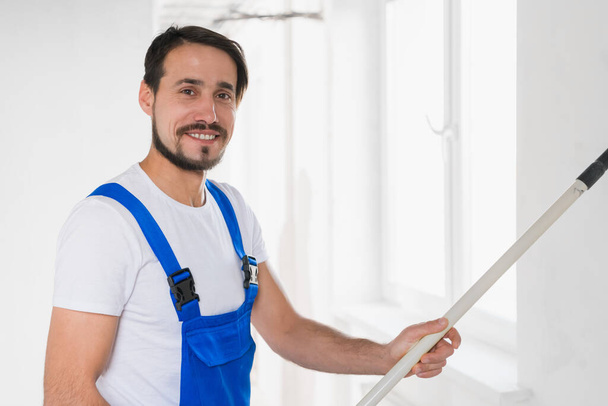 Handsome man in overalls paints the wall with a roller - Photo, Image