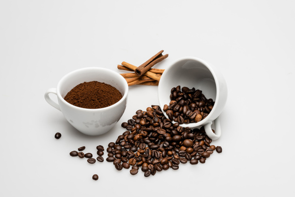 корица палочки возле чашки с молотым кофе и бобы на белом - Фото, изображение