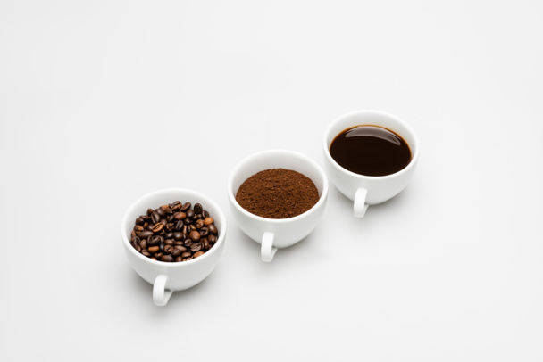canecas com café preparado e moído perto de grãos em branco - Foto, Imagem