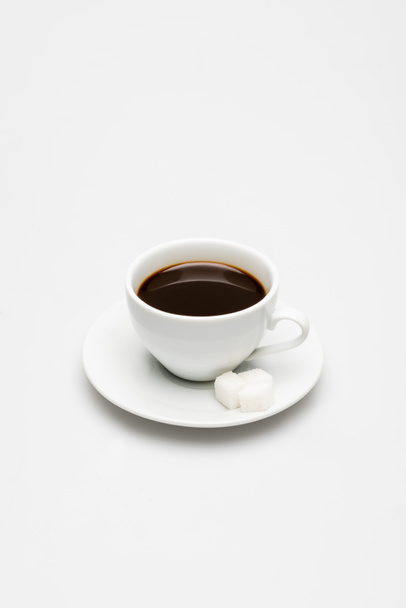 kopje bereide koffie en suikerklontjes op schotel op wit - Foto, afbeelding