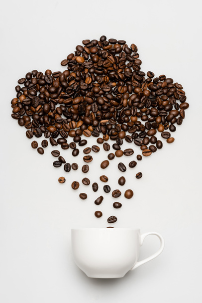 acostado plano con granos de café en forma de nube y lluvia cerca de taza en blanco - Foto, imagen