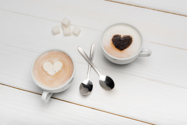 widok z góry kubki z cappuccino i latte w pobliżu łyżek i kostek cukru na białej drewnianej powierzchni  - Zdjęcie, obraz