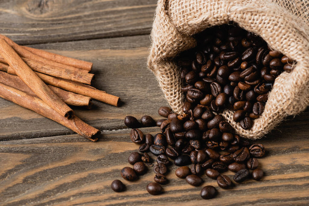 палички кориці біля мішків зі смаженими кавовими зернами на дерев'яній поверхні
  - Фото, зображення