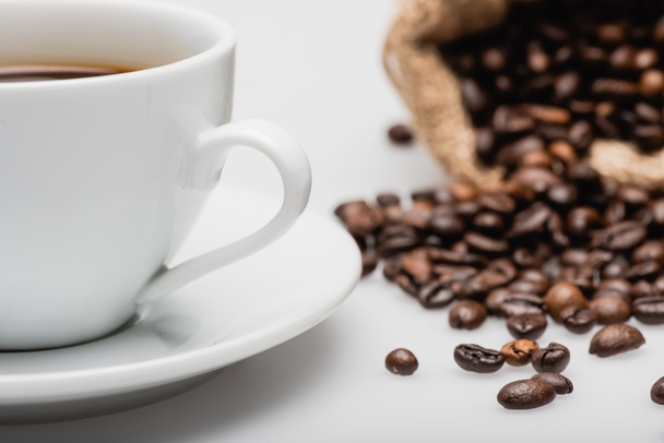 чашка біля мішків зі смаженими кавовими зернами на білому
 - Фото, зображення