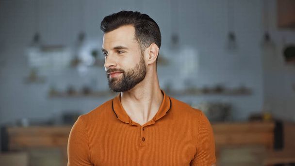 Lächelnder Mann in orangefarbenem T-Shirt schaut im Café weg - Foto, Bild