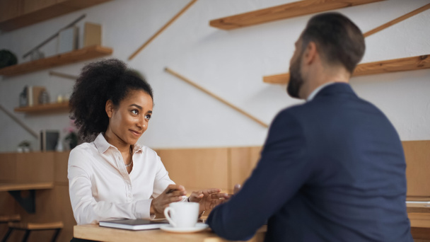 positieve Afro-Amerikaanse zakenvrouw praten met wazig partner tijdens vergadering in cafe  - Foto, afbeelding