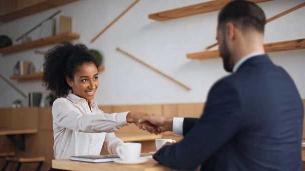 heureux interracial partenaires d'affaires serrant la main lors de la réunion dans le café  - Photo, image