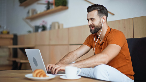homme gai écouter de la musique dans les écouteurs et en utilisant un ordinateur portable dans le café - Photo, image
