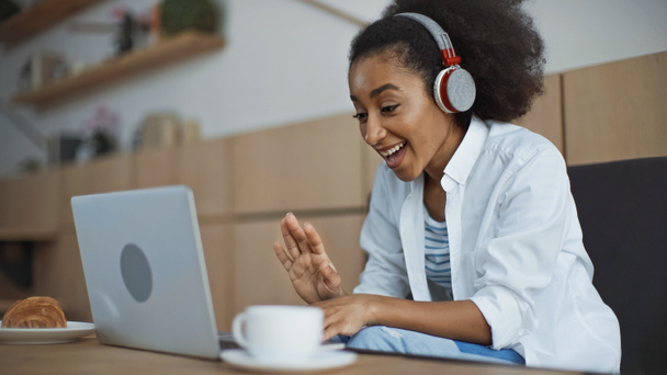 heureuse femme d'affaires afro-américaine dans les écouteurs sans fil ayant chat vidéo dans le café - Photo, image