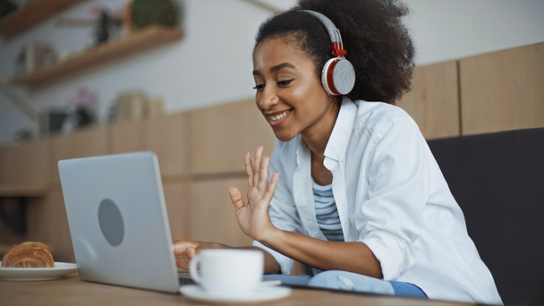 szczęśliwy afrykański amerykański bizneswoman w bezprzewodowy słuchawki mając wideo rozmowy w kawiarni - Zdjęcie, obraz