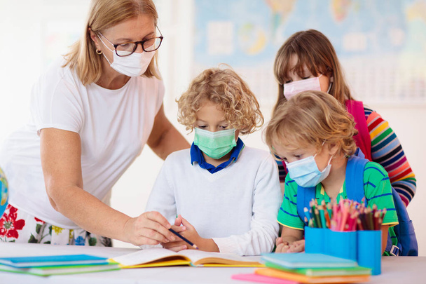 Δάσκαλος στην τάξη, σχολιαρόπαιδο με μάσκα προσώπου κατά τη διάρκεια του ιού του κόρωνα και ξέσπασμα γρίπης. Αγόρι και κορίτσι πίσω στο σχολείο μετά την καραντίνα και τον αποκλεισμό του Covid-19. Ομάδα παιδιών με μάσκες για την πρόληψη του ιού της στέψης. - Φωτογραφία, εικόνα
