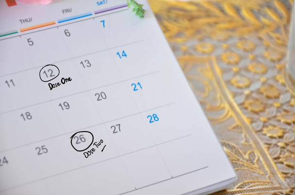 Fehér asztali naptár, amelynek időpontja az orvos számára a kovid-19 vakcina beadásának időpontja, a kovid-19 vakcina naptárban szereplő emlékeztető koncepciója. - Fotó, kép