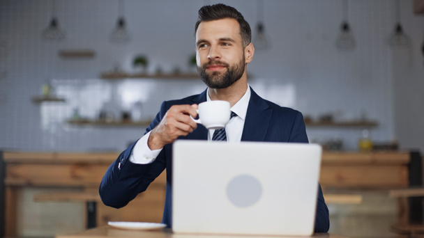 uomo contento in tuta che tiene la tazza di caffè vicino a computer portatile in caffè - Foto, immagini