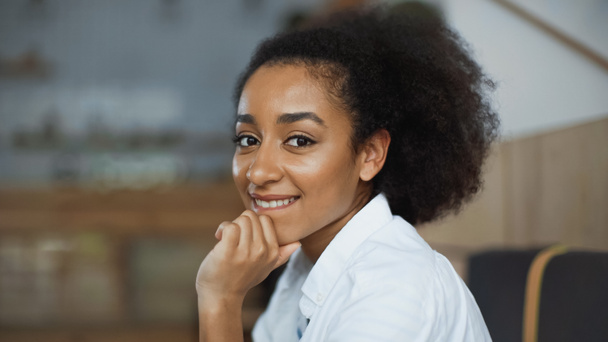 Kafede gülümseyen ve dudaklarını ısıran mutlu Afro-Amerikan kadını. - Fotoğraf, Görsel