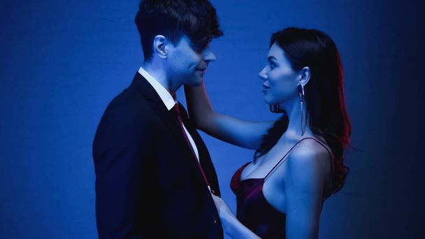vue latérale d'une femme séduisante embrassant un homme souriant en blazer sur bleu - Photo, image