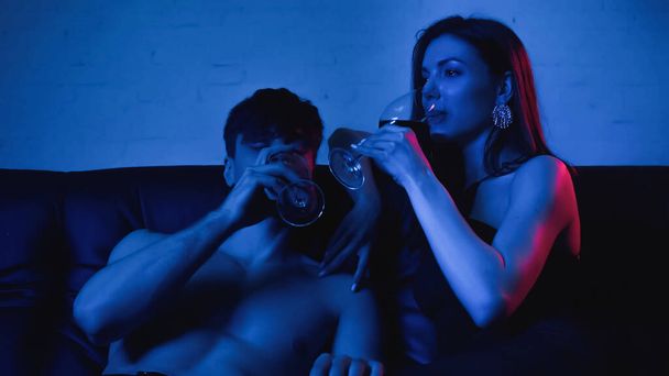 sexy couple holding glasses while drinking wine on blue  - Foto, afbeelding