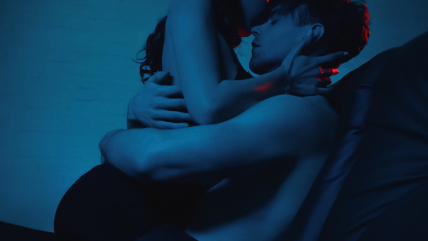 shirtless man with closed eyes hugging sexy woman on black sofa on blue - Foto, afbeelding