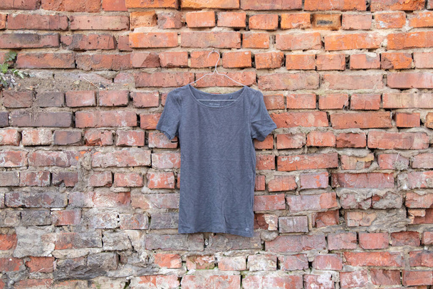 femme t-shirt gris accroché à un cintre sur un mur de briques dans la rue, vêtements pour femmes - Photo, image