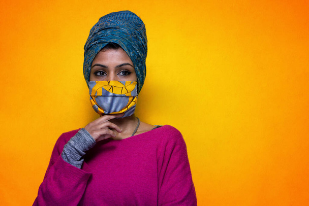 Mulher indiana bonita posando com proteção de máscara 19 covid vestindo um turbante - Menina bonita Sri Lanka usa proteção contra a gripe pandêmica posando com um fundo amarelo - Foto, Imagem