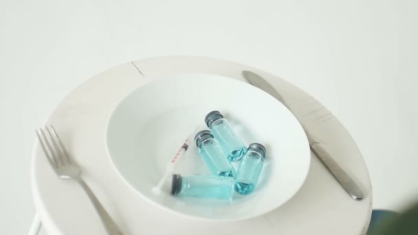 青い液体が入ったガラスのアンプルで白いプレートから食べる予定です予防接種のコンセプトトップビュー - 映像、動画