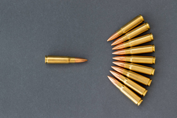 灰色の紙の背景に弾丸、他の前に1発の弾丸。カラシニコフのアサルトライフルの7.62口径。すべての概念に反して - 写真・画像