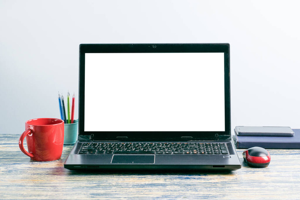 Lugar de trabajo con una maqueta de la pantalla de un ordenador portátil, un teléfono inteligente, un portátil, una taza de té o café, bolígrafos y un ratón de ordenador - Foto, imagen