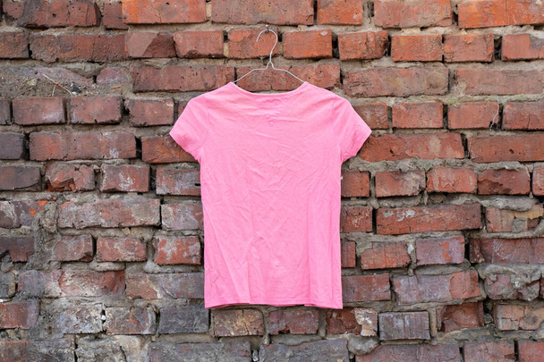 női rózsaszín póló lóg egy vállfán egy téglafalon az utcán, női ruházat - Fotó, kép