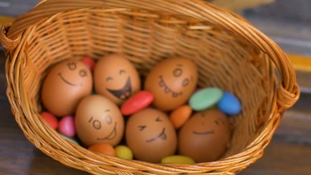 Pila de huevos con caras dibujadas a mano en canasta de paja con dulces de colores, preparación de Pascua, conceptos de humor de vacaciones - Metraje, vídeo
