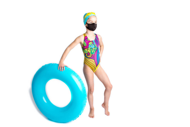 ビーチ水着とインフレータブルターコイズブルーの水泳サークルの愛らしい女の子、黒の保護covid-19マスク.  - 写真・画像