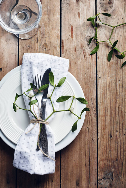 Mise en table. Assiettes blanches, couverts, serviettes et gui sur une table en bois. - Photo, image