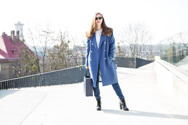 Девушка в синем пальто и сумке гуляет по городу, солнечная погода. - Фото, изображение