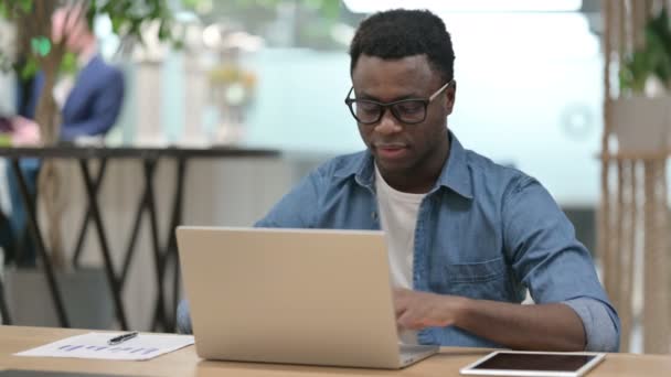 Joven africano sonriendo en la cámara mientras trabaja en el ordenador portátil - Imágenes, Vídeo