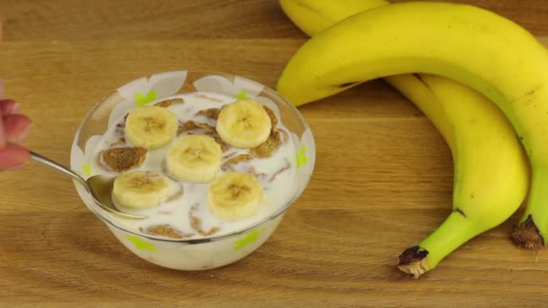 Lähikuva ottaa lusikka hiutaleita täysjyväviljaa maidon ja banaanin hedelmiä. Terveellinen aamiainen tai välipala ruokaa. Terveellisen ruoan käsite. - Materiaali, video
