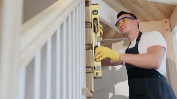 Carpenter installe des escaliers dans une nouvelle maison moderne. Inspecteur masculin de construction vérifier le niveau vertical des pièces d'escaliers par waterpas, examen des escaliers intérieurs de la maison. - Séquence, vidéo