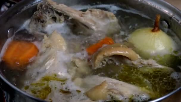 Koken in kokend water vette kippenbouillon van vlees en botten met uien en wortelen voor soepbereiding, in steelpan. Huiselijke keuken. Close-up. - Video