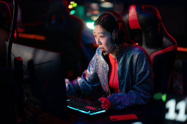 Egy fiatal kínai e-sport játékos egy nemzetközi e-sport versenyen. Egy többfajú cyber csapat online lövöldözős játékot játszik. Neonfény. - Fotó, kép