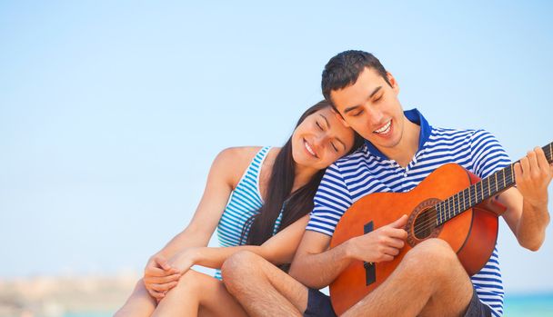 Młoda para z gitarą na plaży w letni dzień. - Zdjęcie, obraz