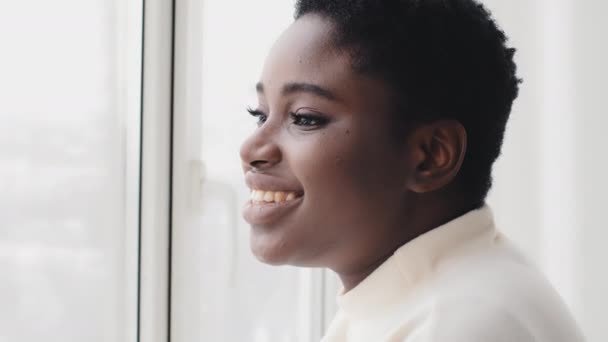 Портрет афро-американської дівчини етнічна чорна жінка профіль дивлячись у вікно, стоячи в денному світлі, насолоджуючись видом, мріючи про майбутні плани, посміхаючись споглядати вранці вдома в приміщенні - Кадри, відео