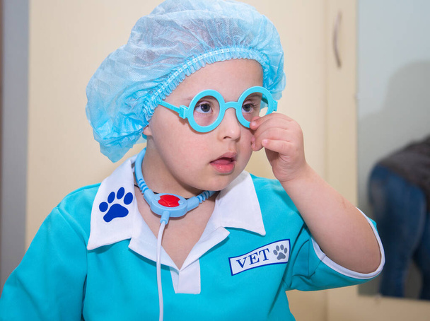 Αγόρι με σύνδρομο Down, πορτρέτο ενός γενετικά άρρωστου ανάπηρου παιδιού με στολή γιατρού, ειδικά παιδιά, γενετικές ανωμαλίες. - Φωτογραφία, εικόνα