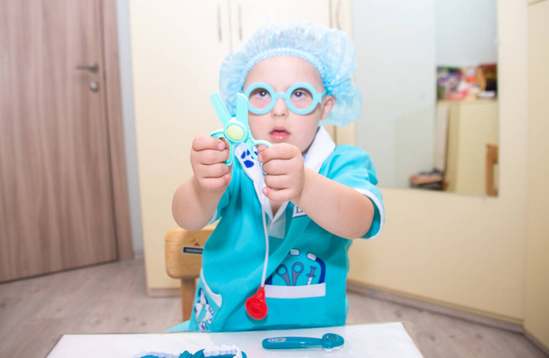 Um menino com síndrome de Down joga como um médico, uma criança com um traje de médico, crianças com deficiência. - Foto, Imagem