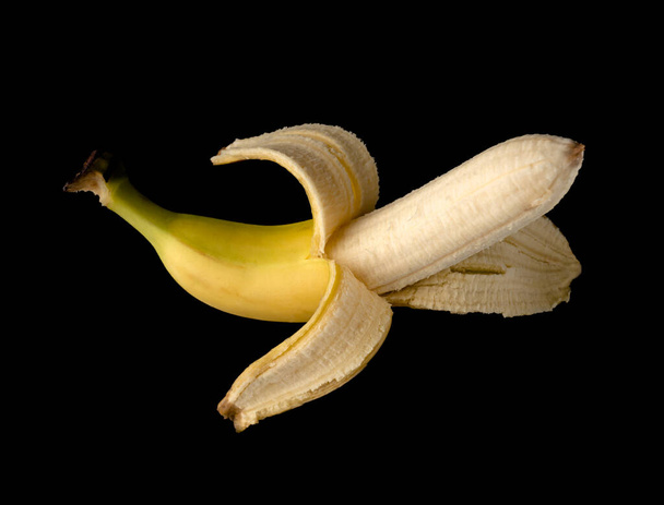 Una banana, mezza sbucciata, su fondo nero, isolata - Foto, immagini