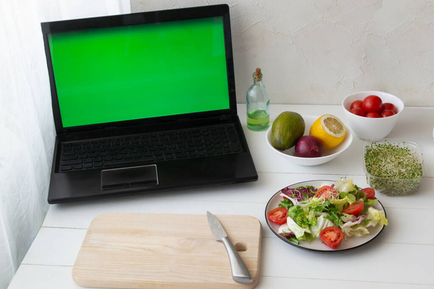 Laptop com cromakey e salada vegetariana verde em um prato branco com ingredientes na mesa. Conceito de cozinha online. Orientação horizontal. - Foto, Imagem