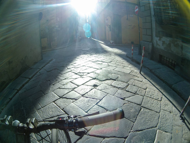 Jazda brukowanymi uliczkami centrum starej Florencji na rowerze, podróż Włochy. Widok pierwszej osoby z jasnym słońcem z przodu. Widok kamery działania - Zdjęcie, obraz