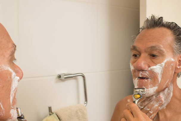 Старший чоловік у ванній з кремом для гоління на обличчі гоління
 - Фото, зображення