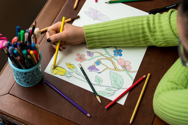 Дівчина в зеленому светрі розмальовує квіти, малюючи на коричневому столі з деякими різними печивами
  - Фото, зображення
