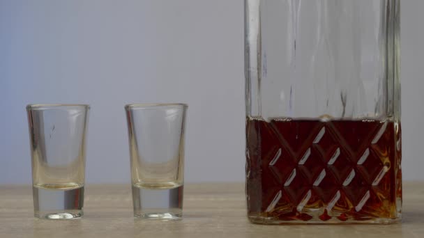 Sobre una mesa de madera hay un decantador en el que el whisky y dos vasos vacíos. Concepto de alcohol y relajación - Imágenes, Vídeo