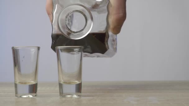 木製のテーブルの上には、ウイスキーと2つの空のグラスが置かれたデカンタが立っており、男の手は液体と飲み物を注ぐ。アルコールとリラクゼーションのコンセプト - 映像、動画
