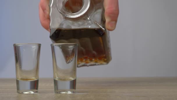 C'è un decanter di vetro di whisky e due bicchieri su un tavolo di legno. La mano dell'uomo prende in mano un decanter e versa il liquido in due bicchieri. Concetto di alcol e relax - Filmati, video
