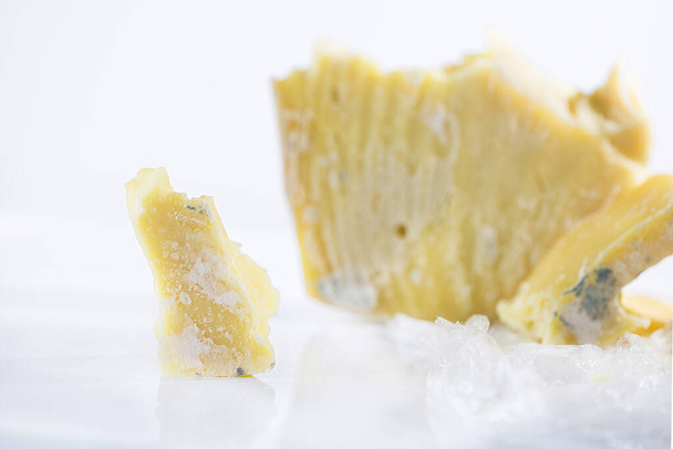 Un morceau de fromage cheddar moisi sur fond blanc, gros plan, macro photographie - Photo, image